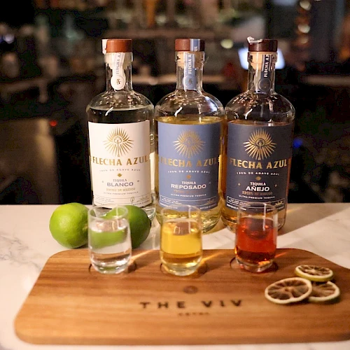A whiskey tasting setup with three bottles and a shot glass on a wooden board, plus lime wedges and citrus garnishes on the board.