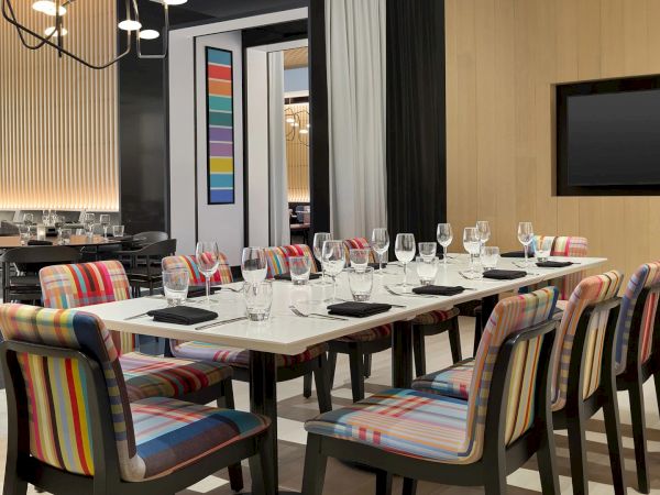 A stylish dining room setup with a long table, cushioned striped chairs, wine glasses, and a modern, colorful decor vibe, perfect for gatherings.