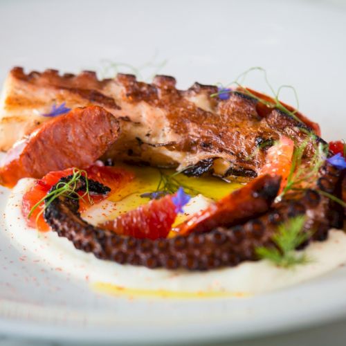 A barbecued corn dog or sausage in a bun with sauce, on a plate (food item with sauce). Top it at 140 characters, always ending the sentence.