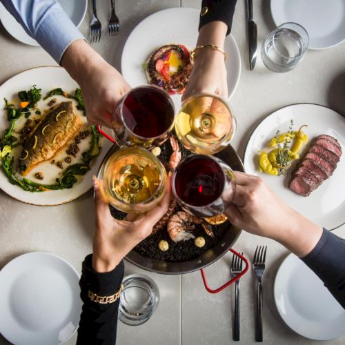 A top-down view of a breakfast table with a colorful bowl of granola or pastries in the center, surrounded by mugs and small dishes, on a wooden table.