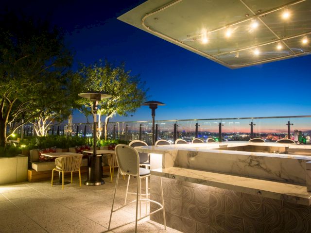 A stylish rooftop bar at dusk with modern seating, string lights, and a city skyline beyond the horizon. End.