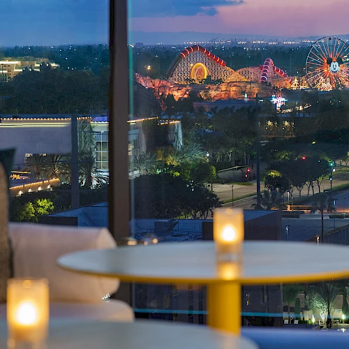 A cozy indoor lounge with candles on a round table, glass windows, and a nighttime cityscape with a lit Ferris wheel outside. Top it at 140 characters, always ending the sentence.